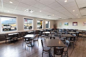 A spacious indoor dining area with multiple tables and chairs, large windows with a view of mountains, and artwork on the walls.