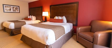 A hotel room with two beds, a brown leather armchair, and a lamp.