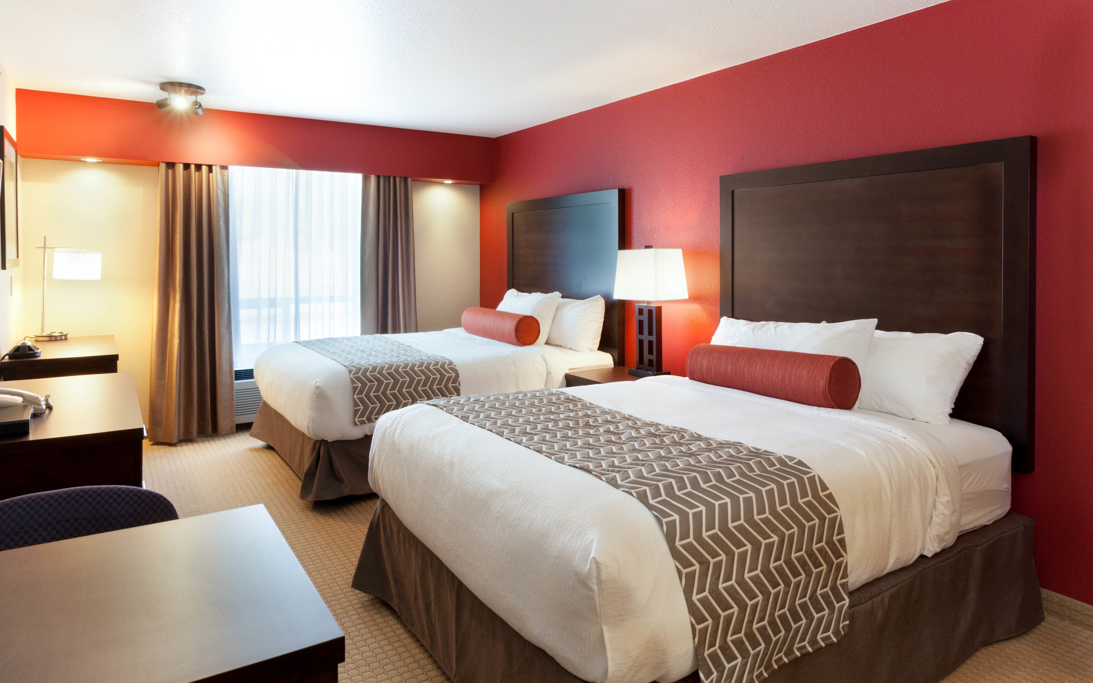 Habitación de hotel con dos camas, un escritorio, una silla y una ventana con cortinas.