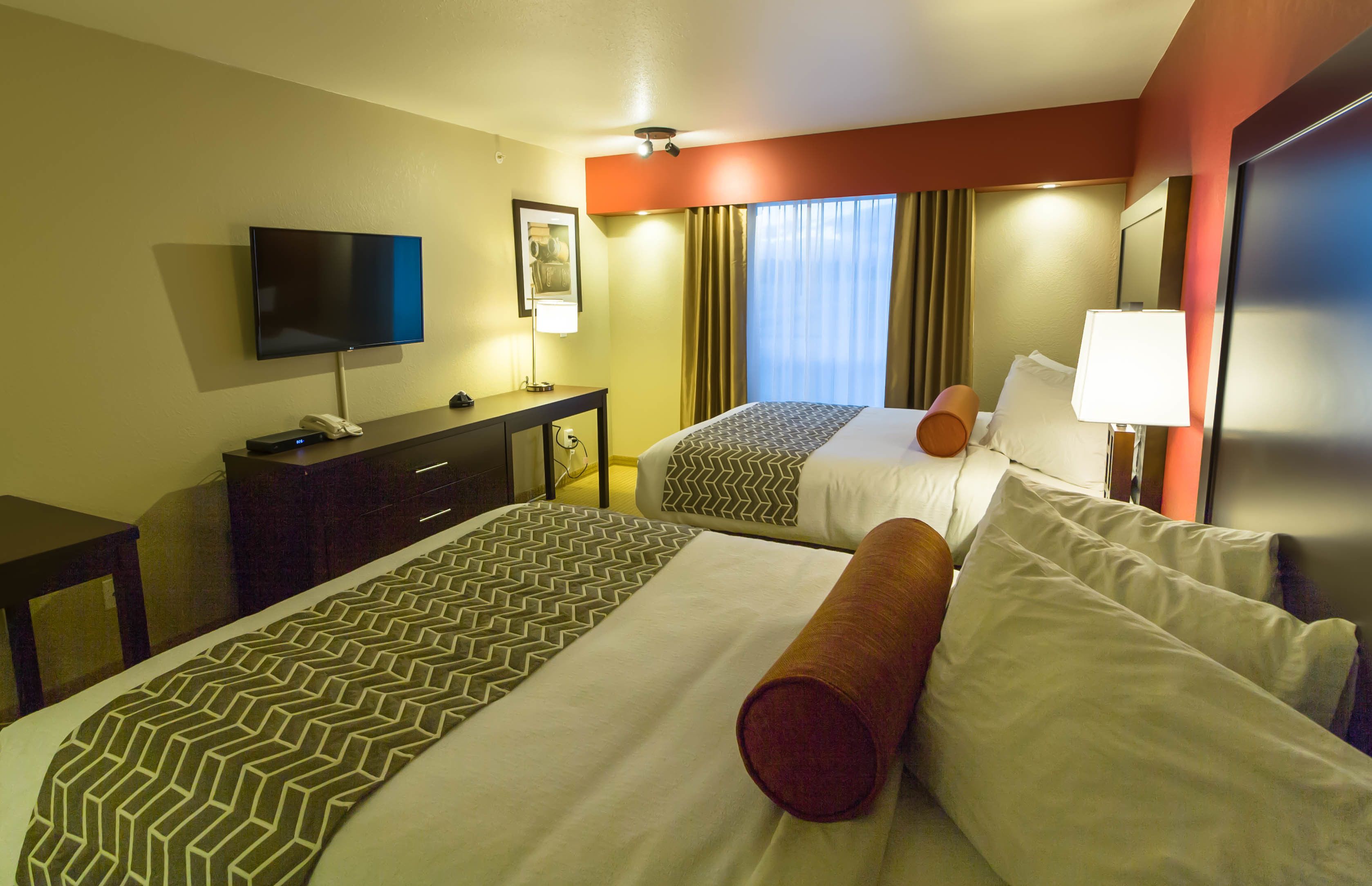 A hotel room with two beds, a TV, a desk, and a window with curtains.