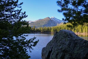 A lake with a mountain in the background, surrounded by dense forest. - The Outpost Rocky Mountains (Estes Park)