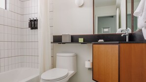 A modern bathroom with a white toilet, a bathtub, a wooden vanity with a sink, and a mirror. - The Outpost Rocky Mountains (Estes Park)