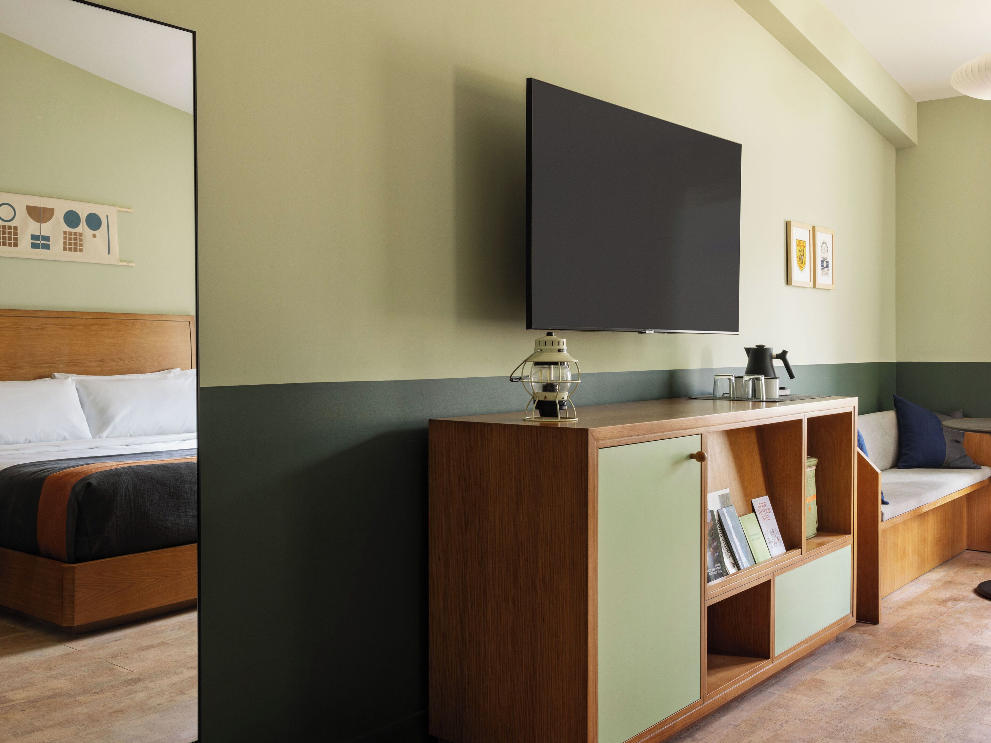 A hotel room with a bed, a wooden console table with a flat-screen TV, a small table with a coffee maker, and a sofa with cushions.