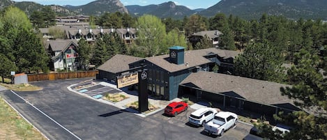 Un hotel con estacionamiento, un letrero que dice 'The Outpost Rocky Mountains' y una montaña al fondo.