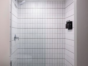 A shower with white tiles, a glass door, and a handheld showerhead. - The Outpost Rocky Mountains (Estes Park)