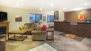 A cozy living room with a fireplace, a sofa, a coffee table, and a reception desk with a Super 8 logo. - Super 8 by Wyndham Jamestown (Jamestown)