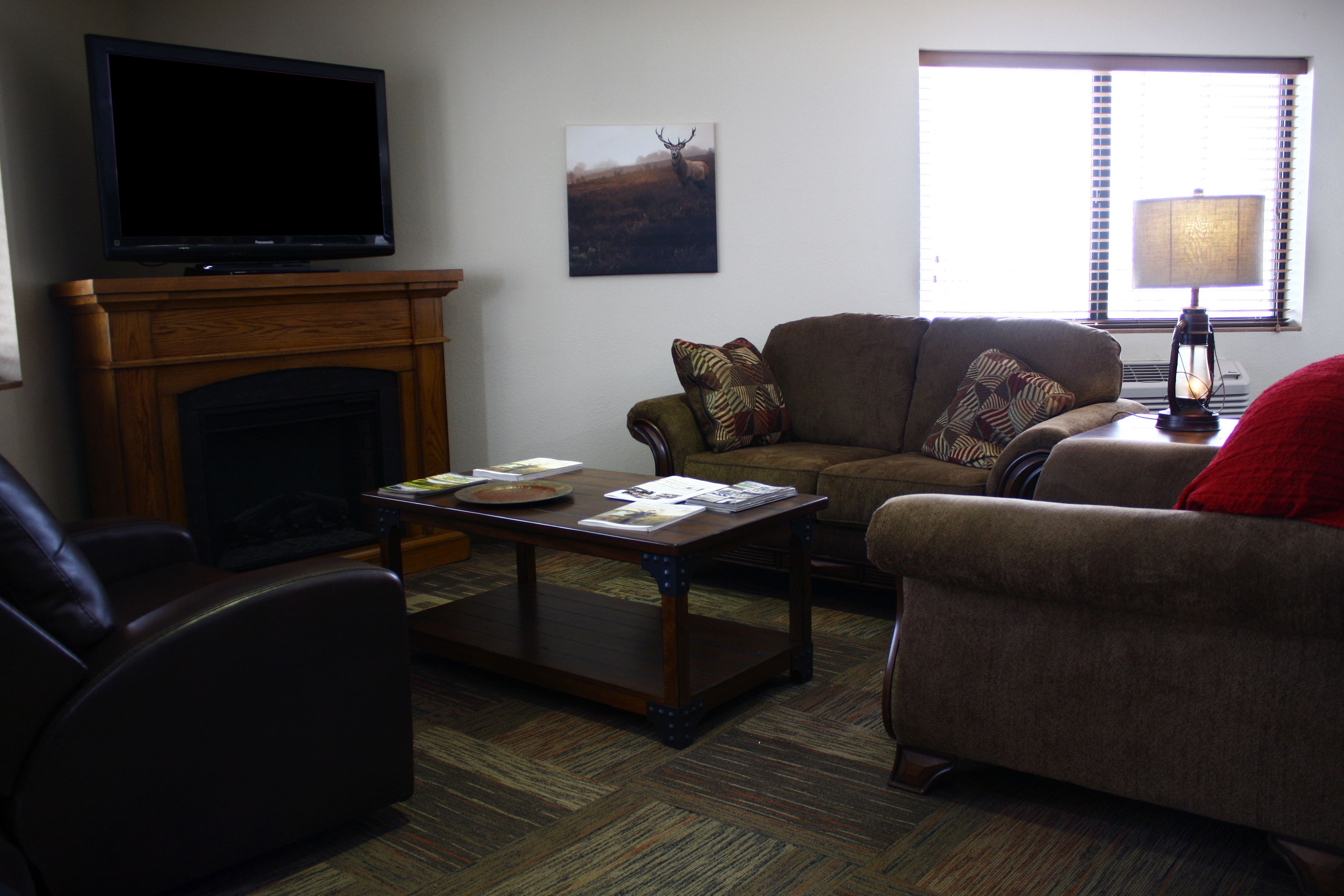 A living room with a fireplace, a television, a sofa, a coffee table, and a window with blinds.