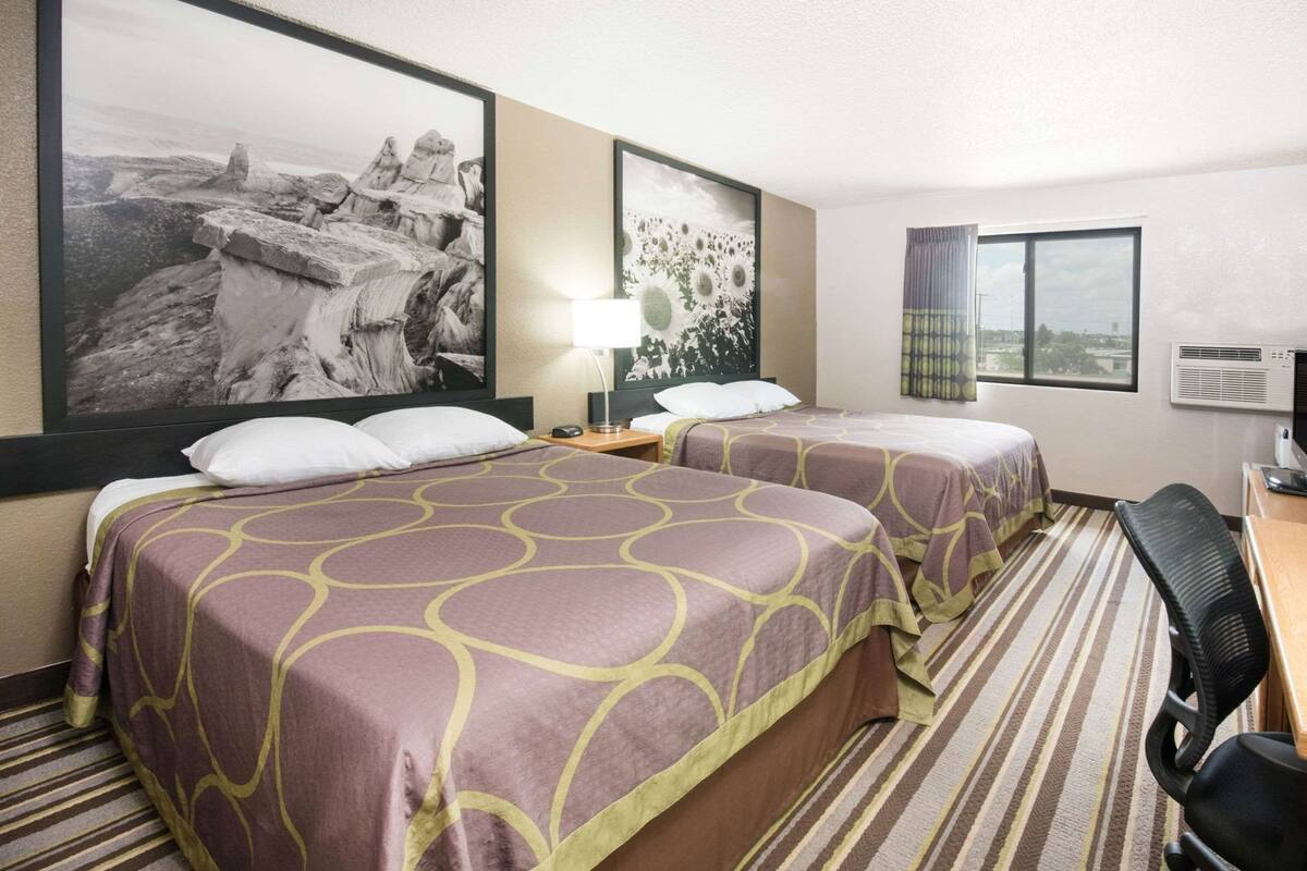 Une chambre d’hôtel avec deux lits, un bureau, une chaise, une lampe et deux grandes images encadrées au mur.