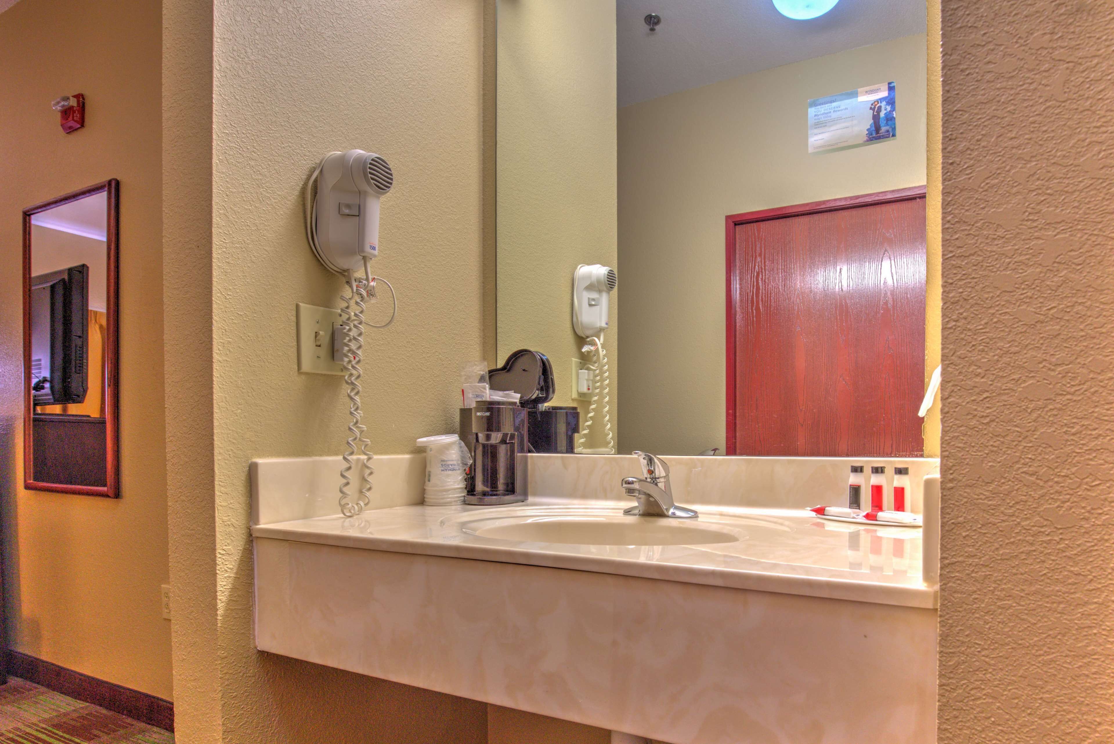 A hotel bathroom with a sink, a hairdryer, and a mirror.