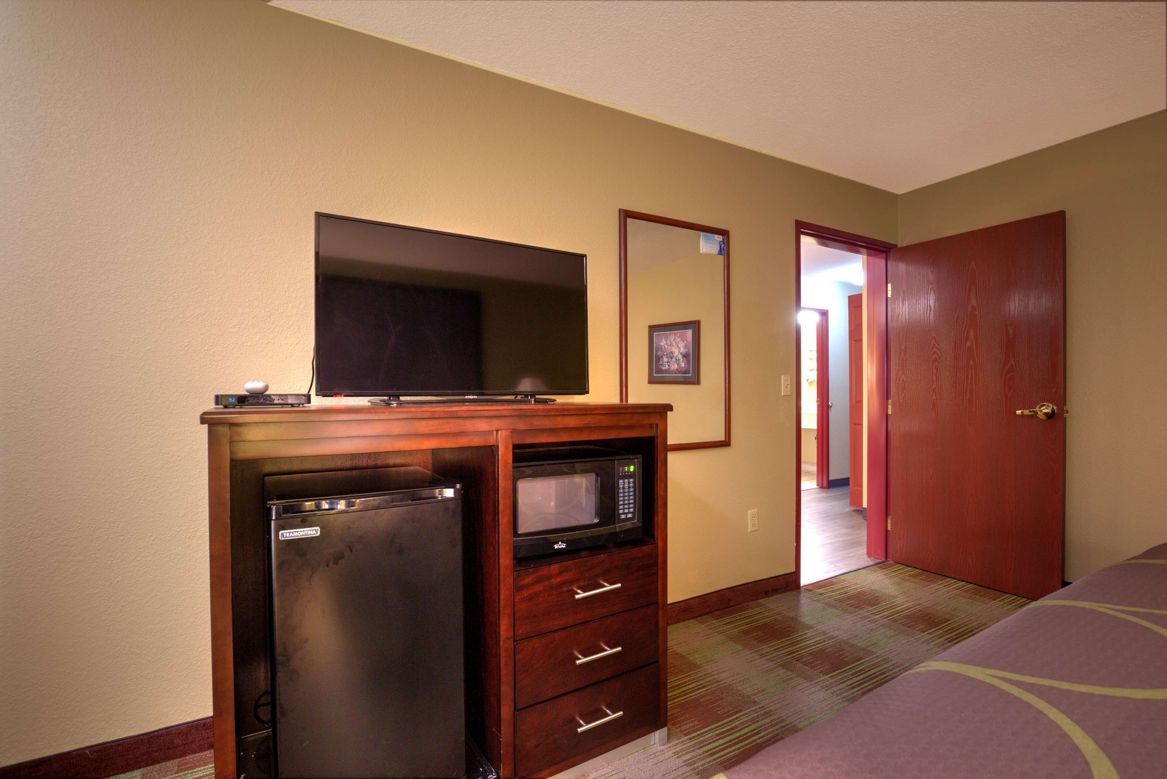 Una habitación de hotel compacta con kitchenette, que incluye un refrigerador y un microondas, una cama, una puerta y piso alfombrado.