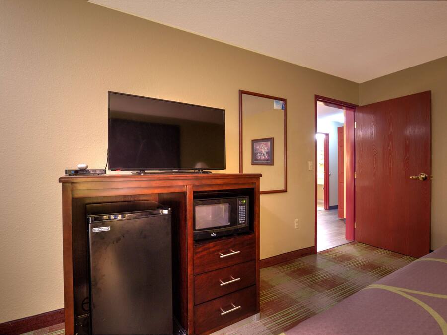 Una habitación de hotel compacta con kitchenette, que incluye un refrigerador y un microondas, una cama, una puerta y piso alfombrado.