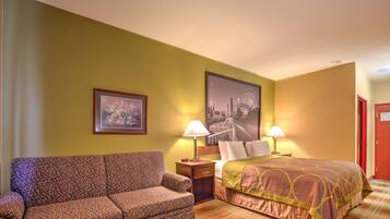 A hotel room with a sofa, a bed with a patterned bedspread, two bedside lamps, a framed picture on the wall, and a large cityscape poster.