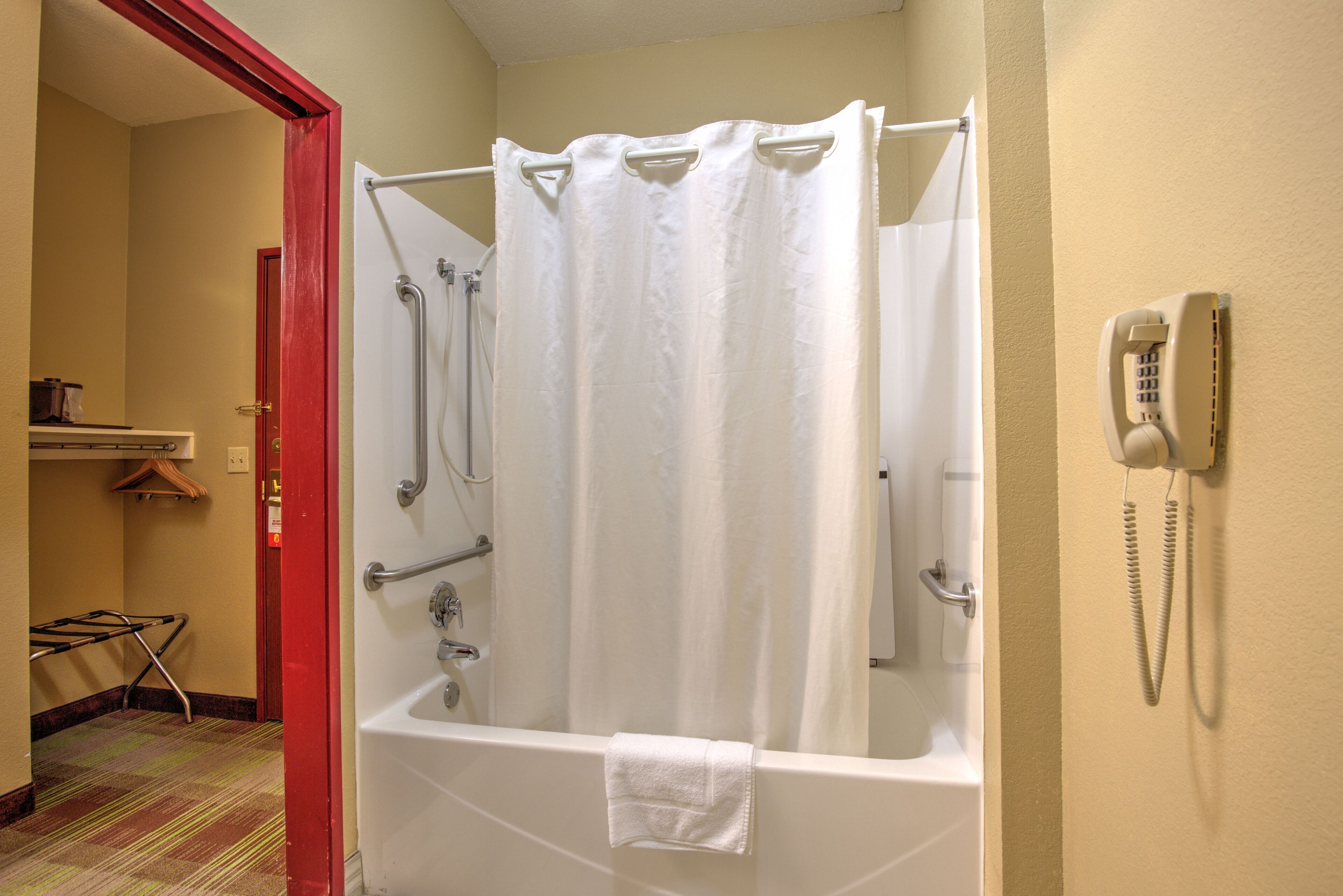 A bathroom with a bathtub, shower curtain, and a telephone mounted on the wall.