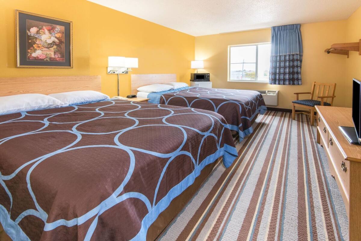 A hotel room with two beds, a television, a desk, and a window with curtains.