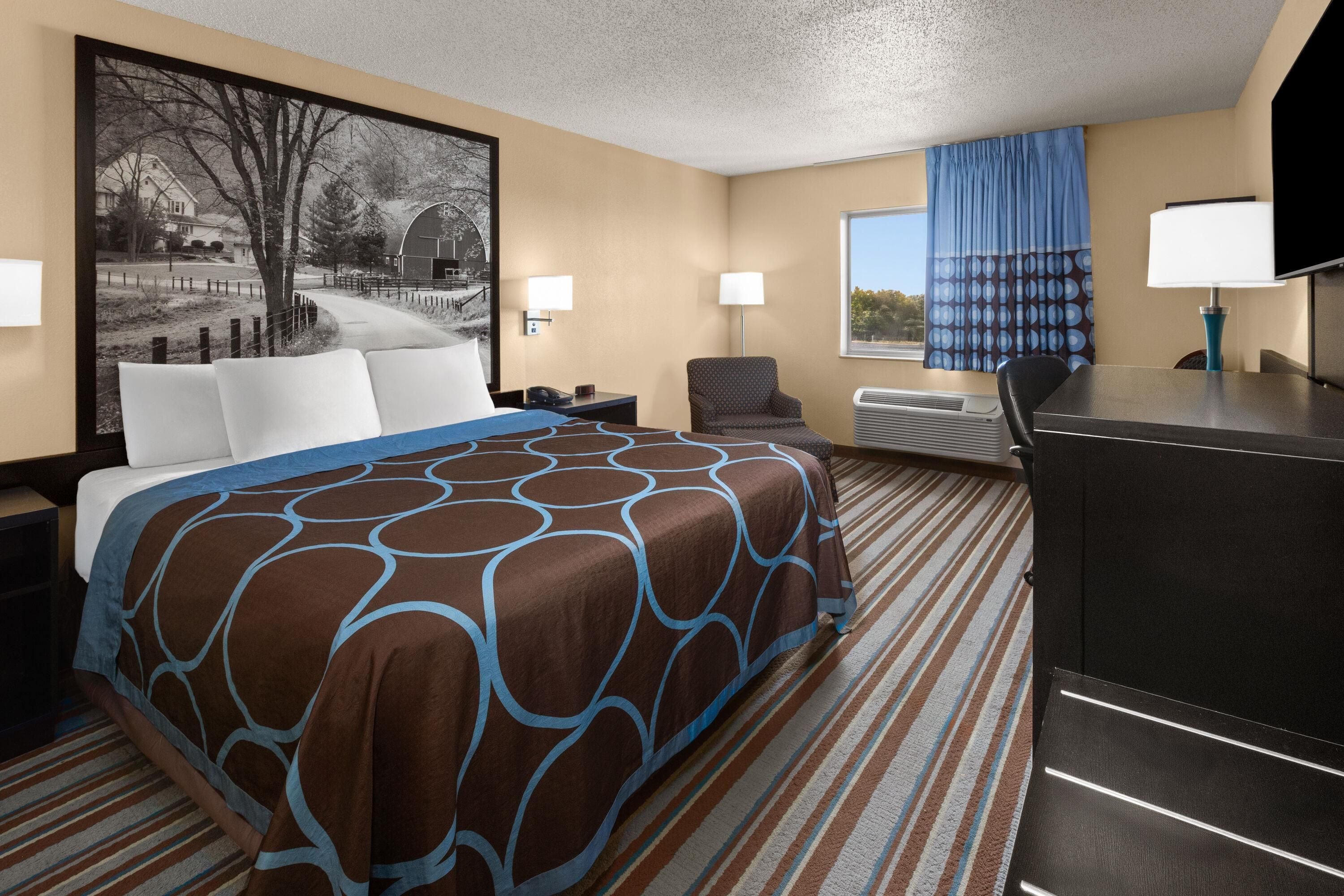 Habitación de hotel con una cama grande, un escritorio, una silla, un televisor de pantalla plana y una ventana con cortinas.