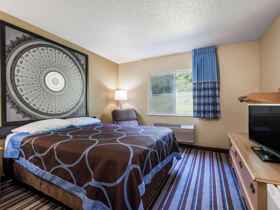 A hotel room with a large bed, a television, a desk, and a window with curtains.