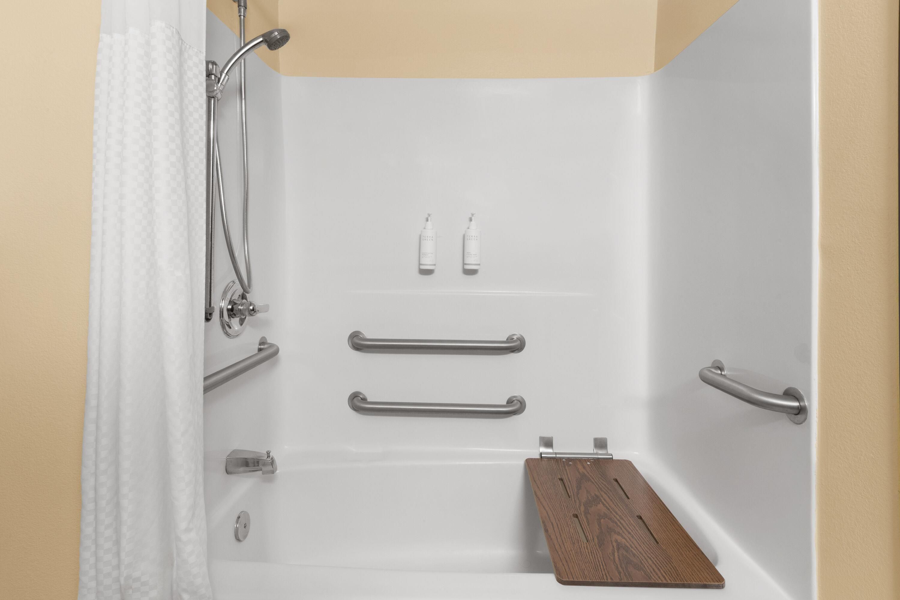 A bathroom with a bathtub, grab bars, a showerhead, and a wooden tray.