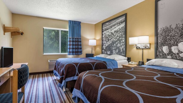 A hotel room with two beds, a desk, a chair, a window with curtains, and a large framed picture on the wall. - Super 8 by Wyndham Medina (Medina)