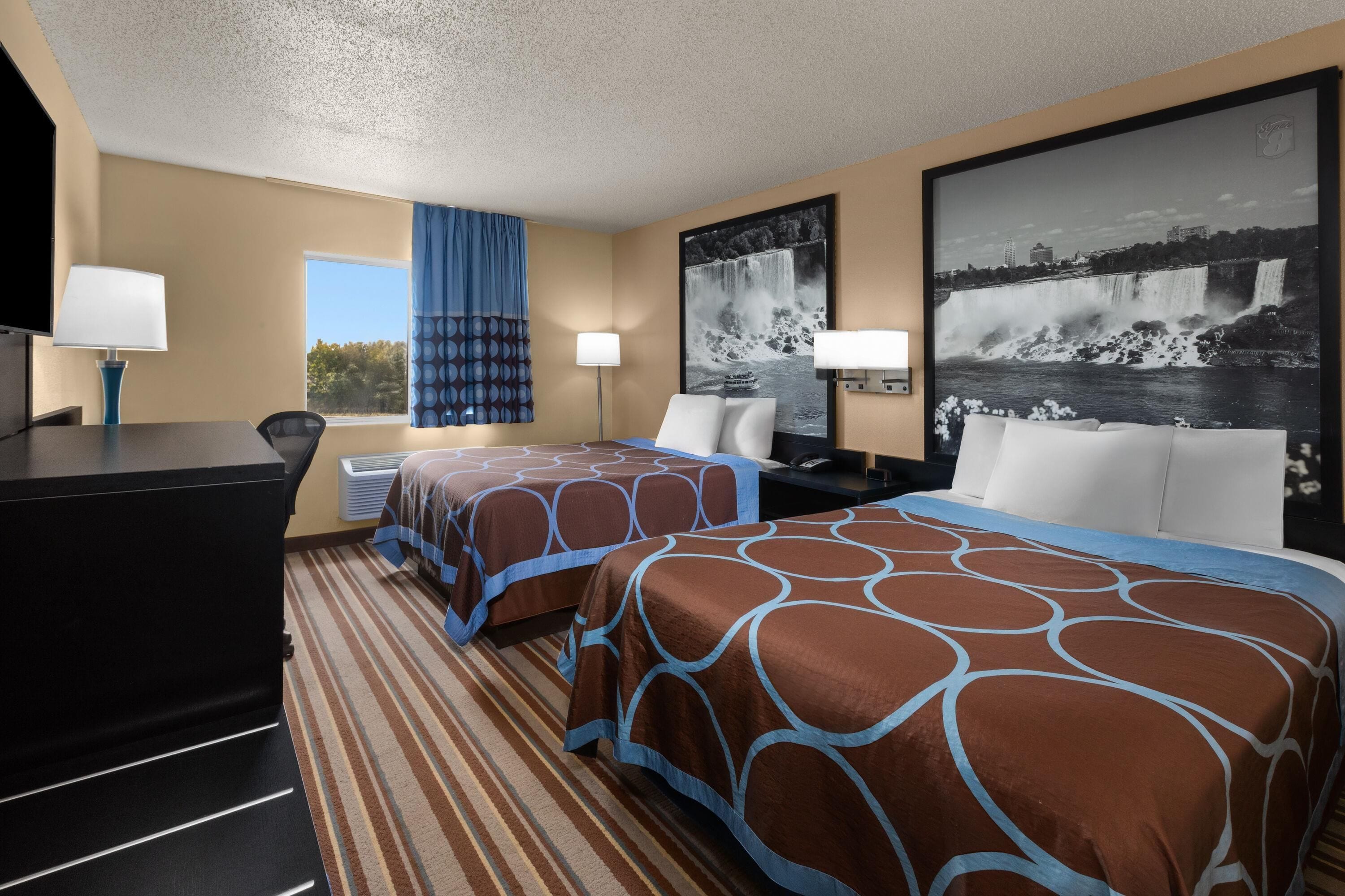A hotel room with two beds, a desk, a TV, and a large window.
