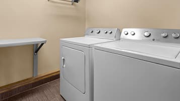 A laundry room with two white front-loading washing machines, a metal towel rack on the wall, and a small table with a metal frame.