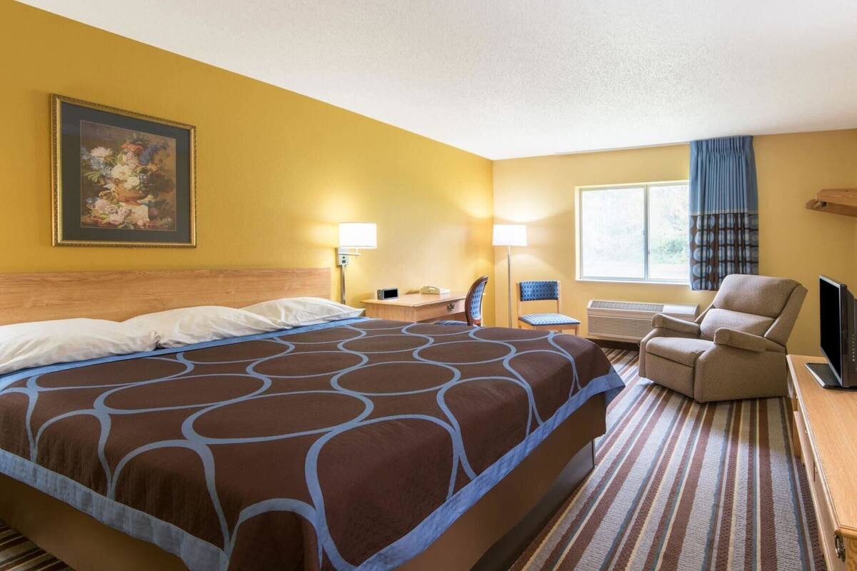 A hotel room with a large bed, a desk with a chair, a TV, and a window with curtains.