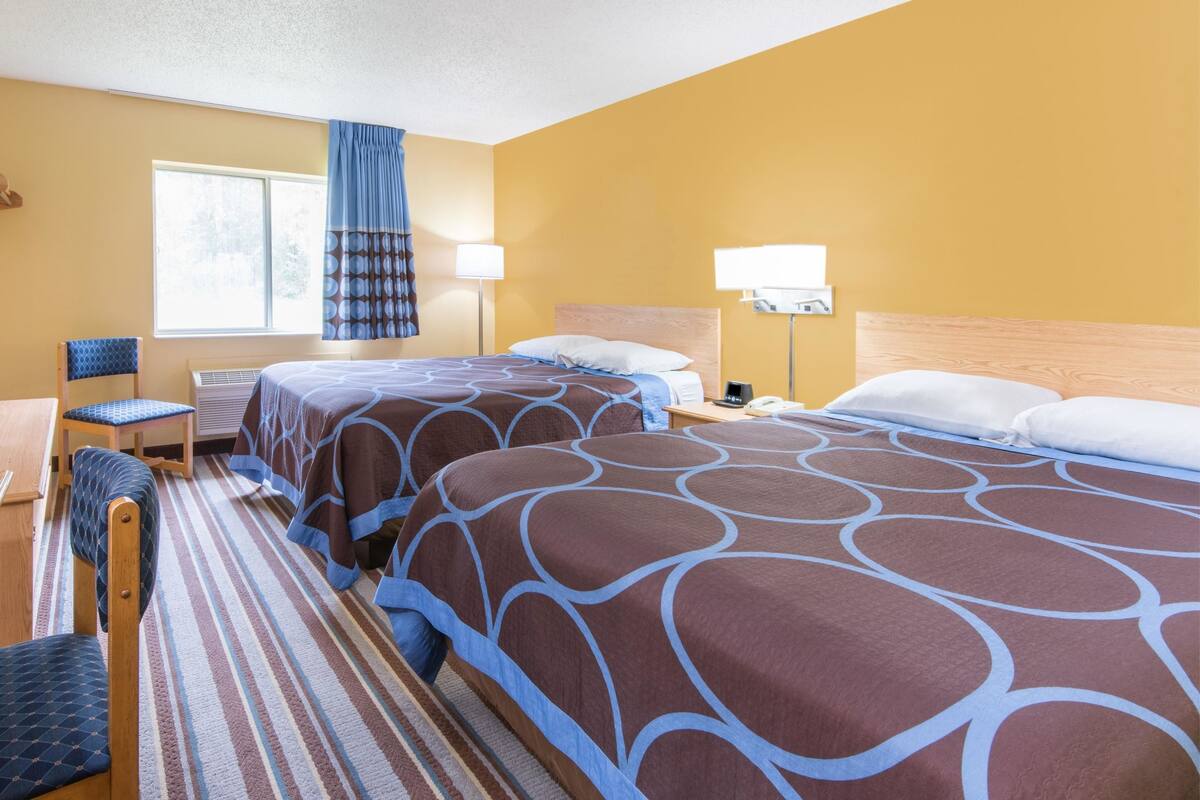 A hotel room with two beds, a desk, a chair, and a window with curtains.