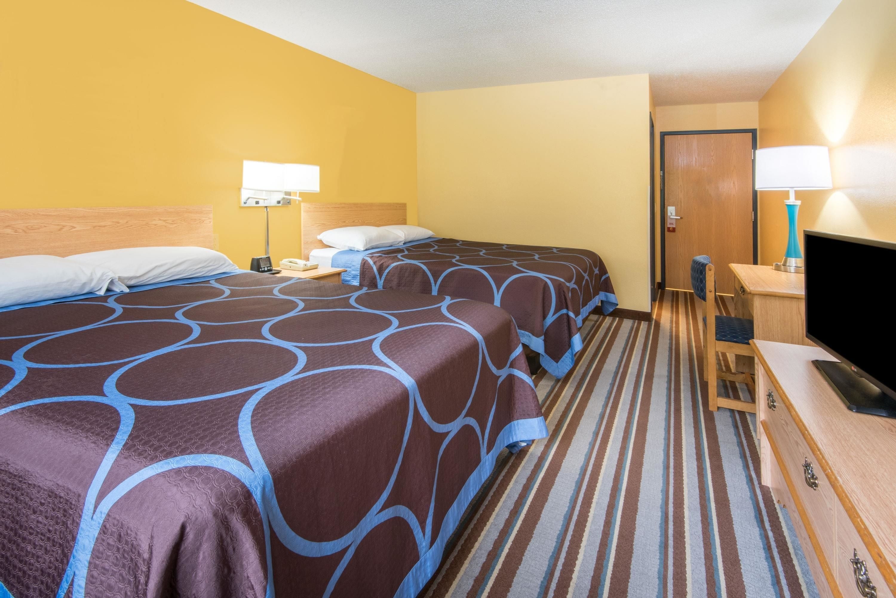 A hotel room with two beds, a desk with a computer, a TV, and a door.