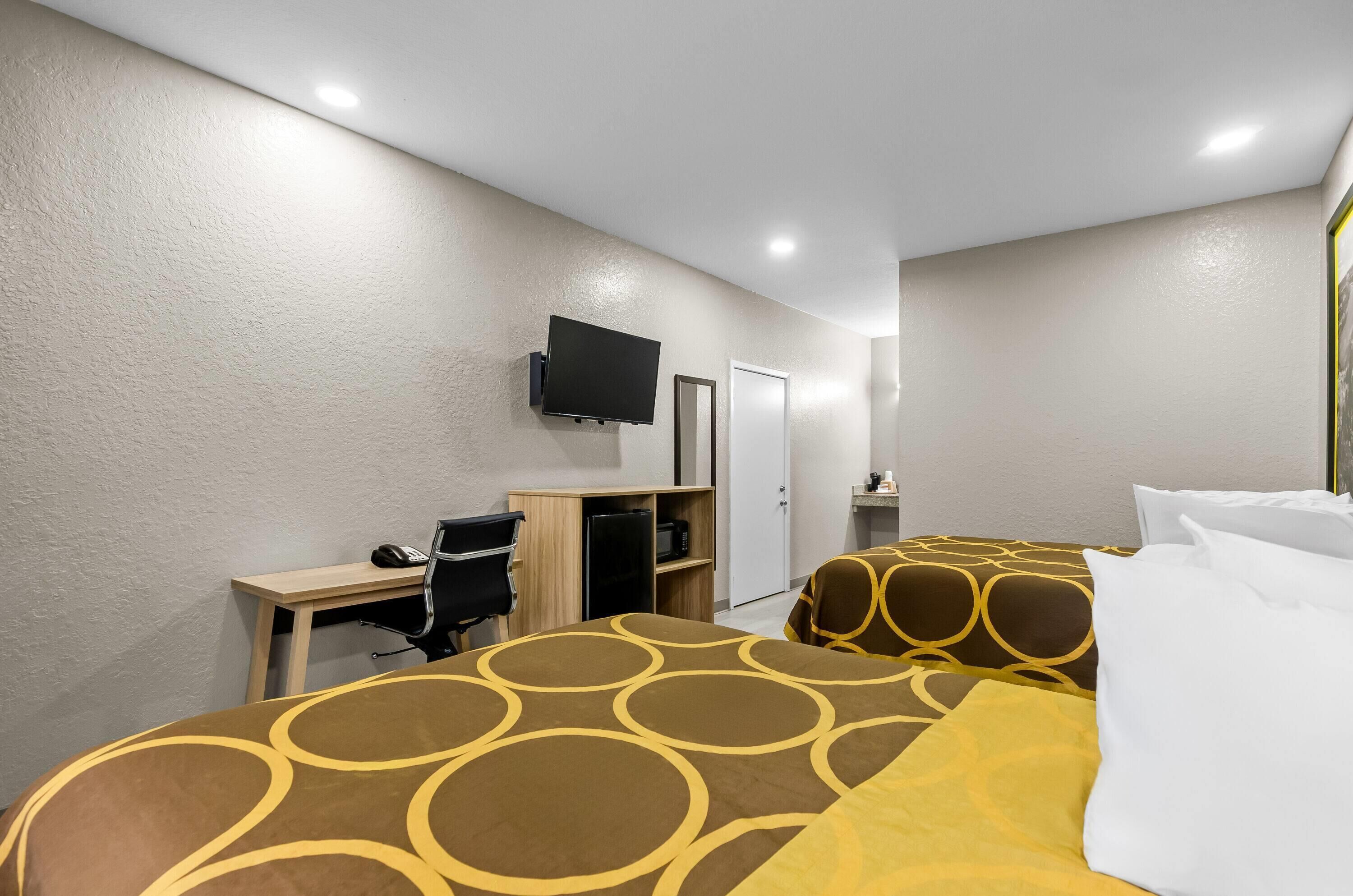Habitación de hotel con dos camas, un escritorio, una silla, un televisor y una puerta.