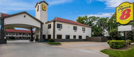 A Super 8 motel with a central tower, a covered parking area, and a clear sky.