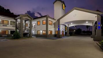 A hotel with a central entrance, multiple balconies, and a parking area.