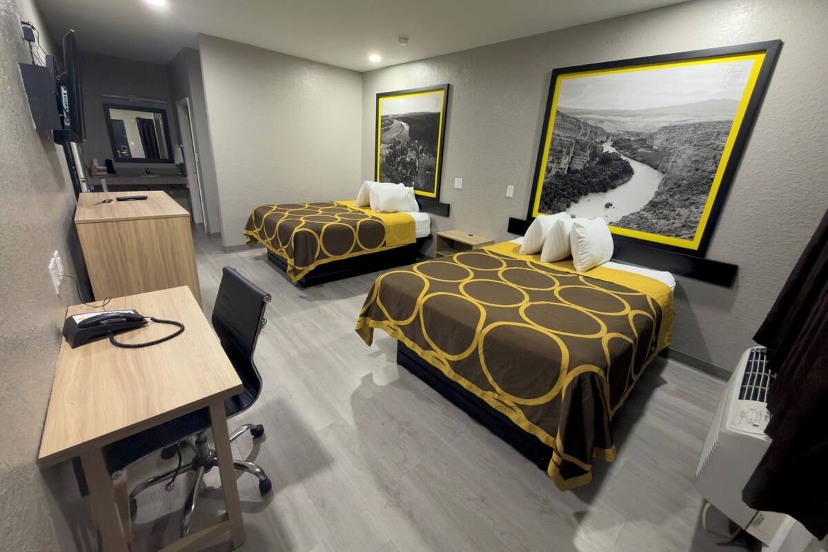 A hotel room with two beds, a desk, and a chair. There are two framed pictures on the wall.