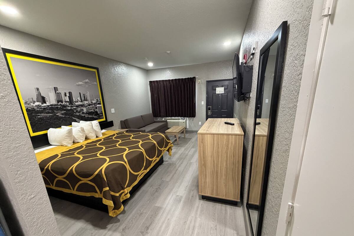 A modern hotel room with a large bed, a small desk, a TV, and a cityscape mural on the wall.