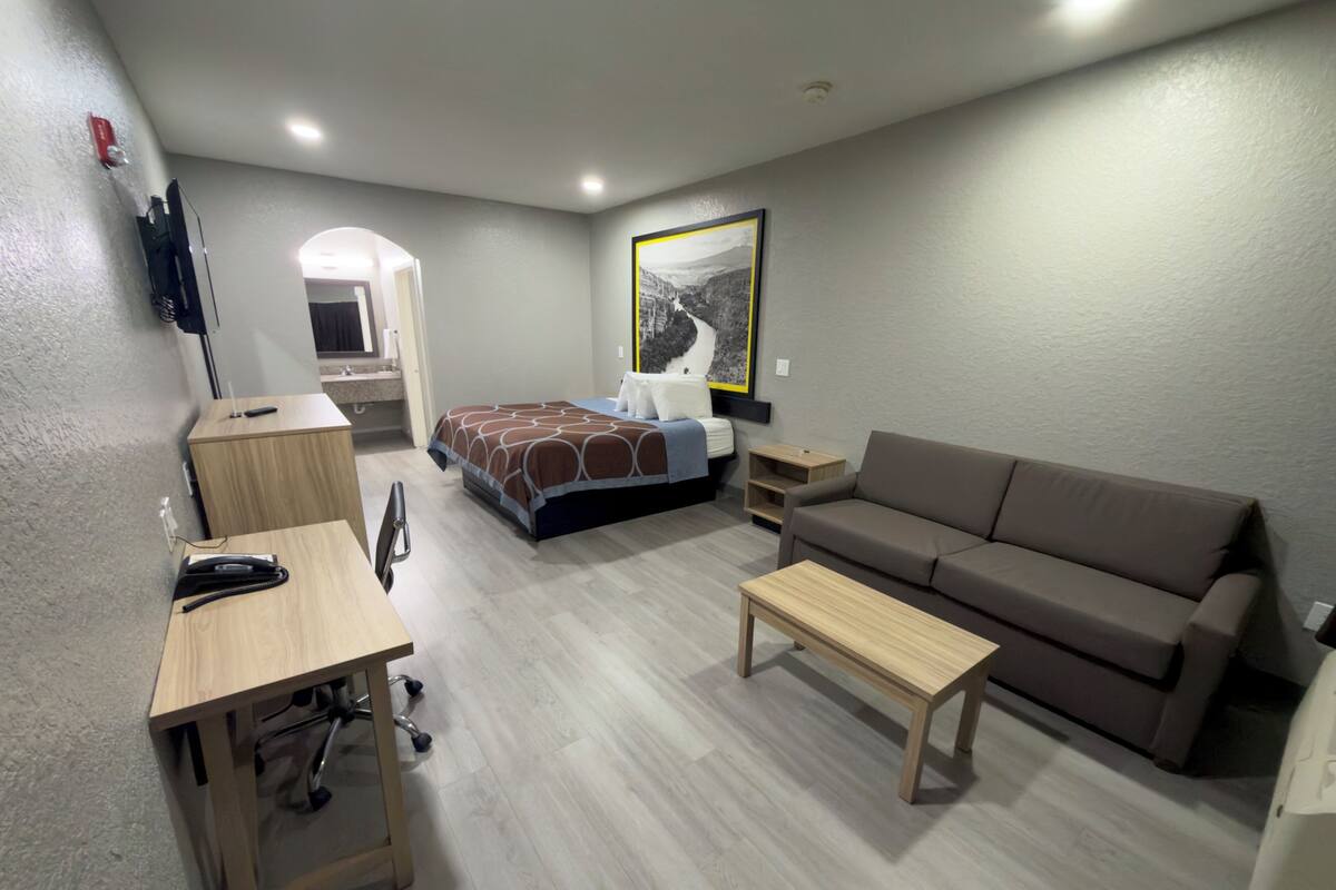 A compact hotel room with a bed, a sofa, a desk, and a small table.