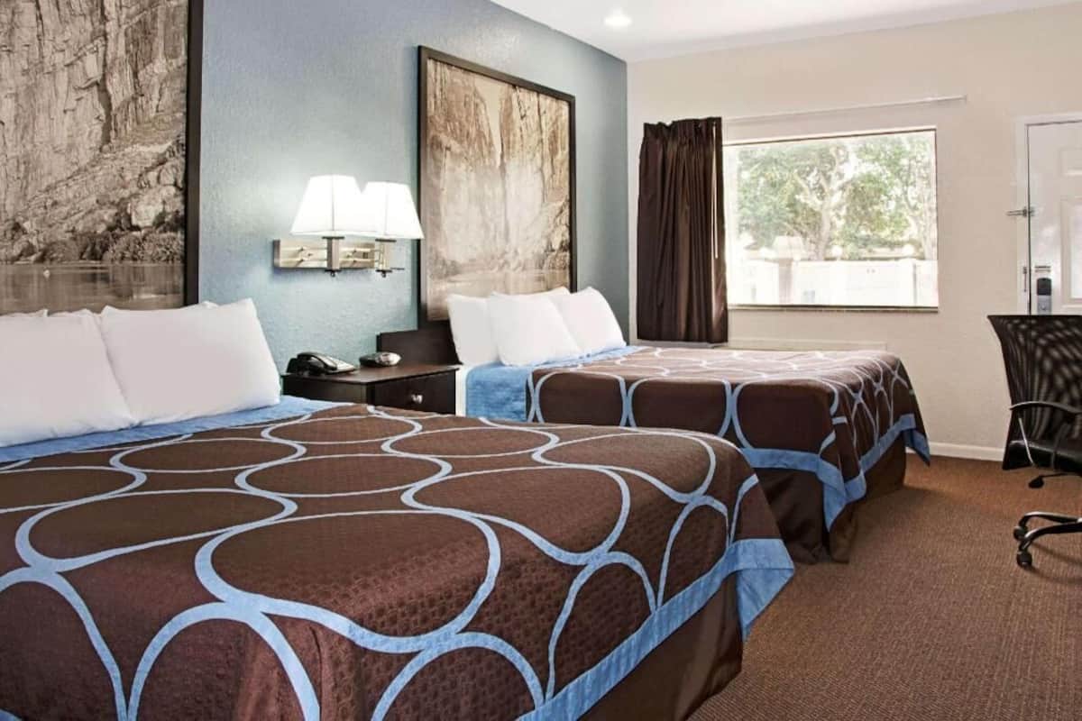 A hotel room with two beds, a desk, a chair, a lamp, and a large window.