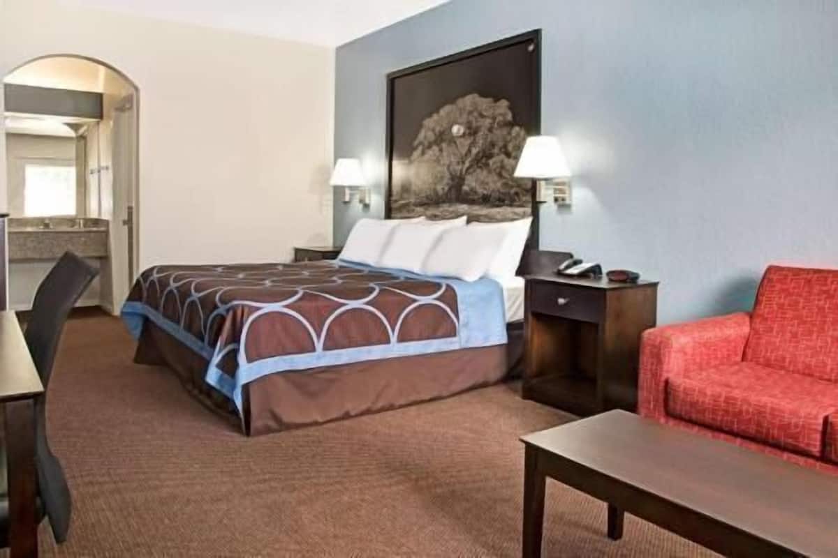 A hotel room with a bed, a desk, a chair, a red sofa, and a painting on the wall.