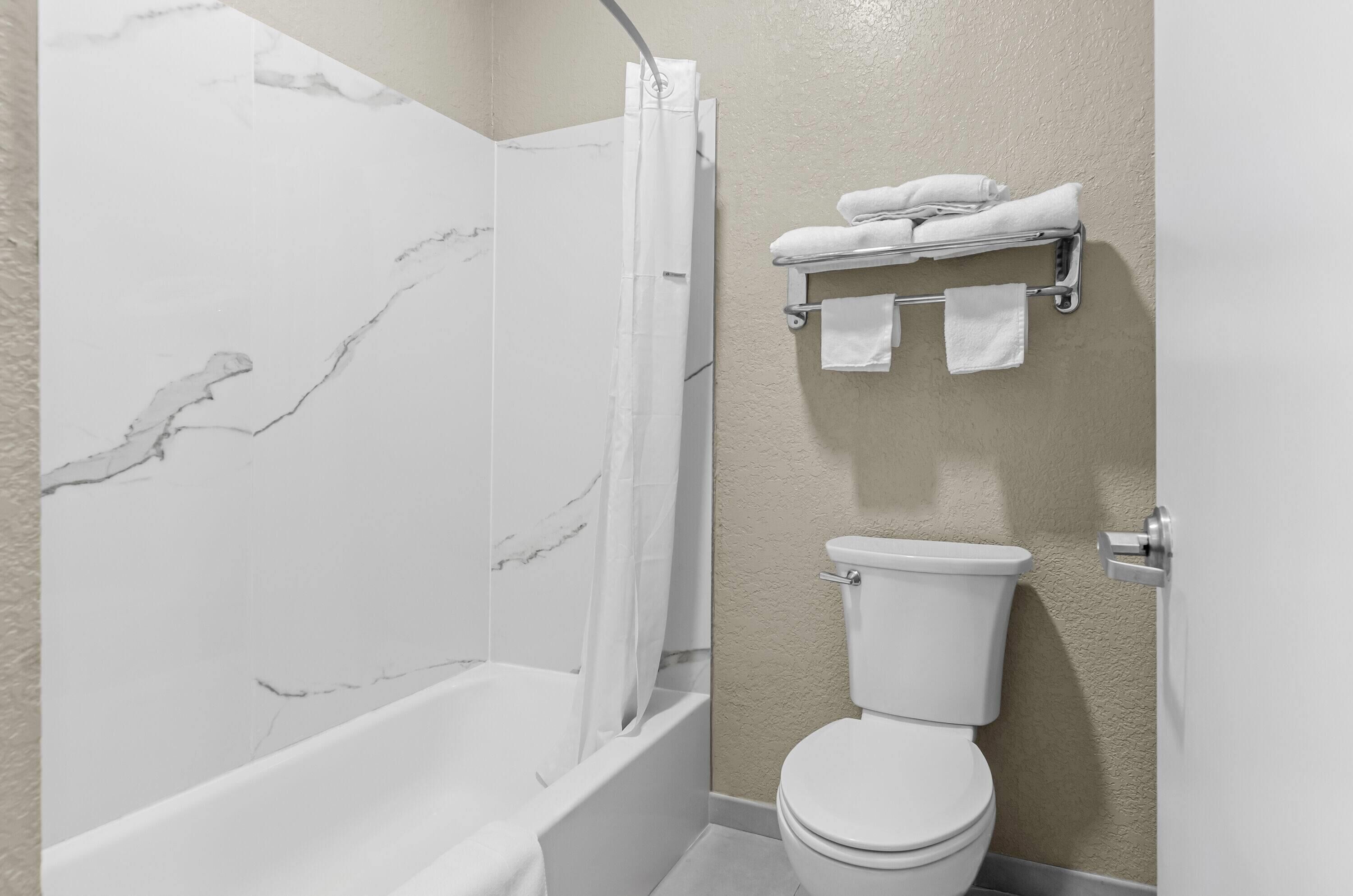 Baño con pared de ducha de mármol, inodoro y toallero con toallas.