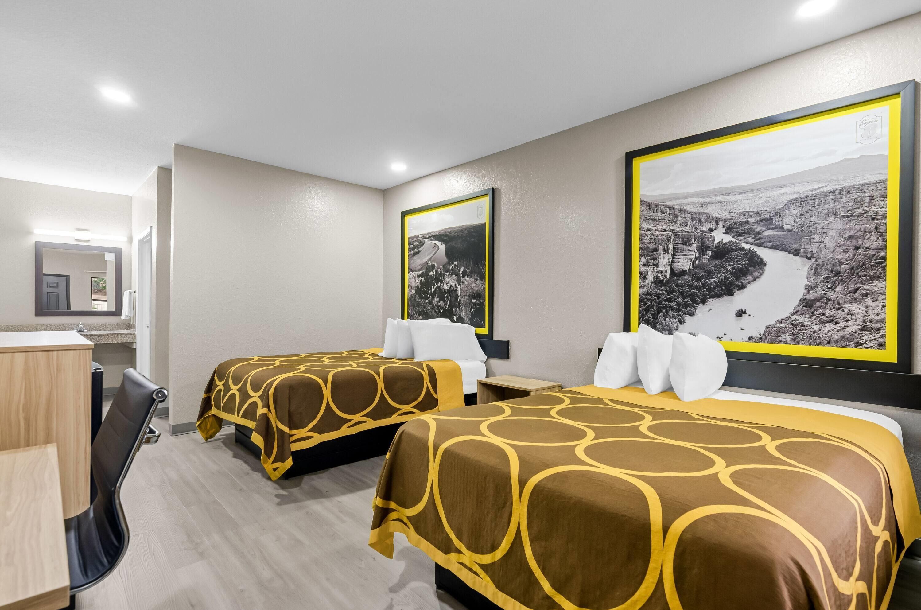 A hotel room with two beds, a desk, and a mirror.