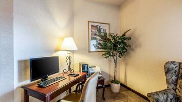 Une chambre d’hôtel équipée d’un bureau, d’un ordinateur, d’une lampe, d’une chaise et d’une plante en pot.