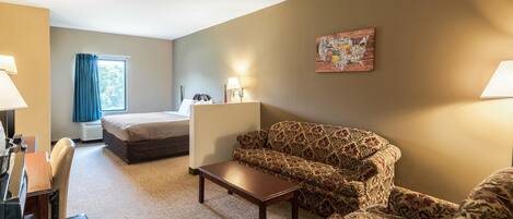 A hotel room with a bed, a sofa, a coffee table, a desk, and a lamp.
