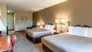 A hotel room with two beds, a desk, a chair, and a lamp.