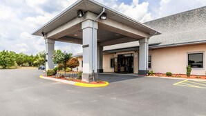 Ein Hotel mit Eingangsbereich, überdachtem Zugang, Parkplatz und einem Gebäude mit grauem Dach.