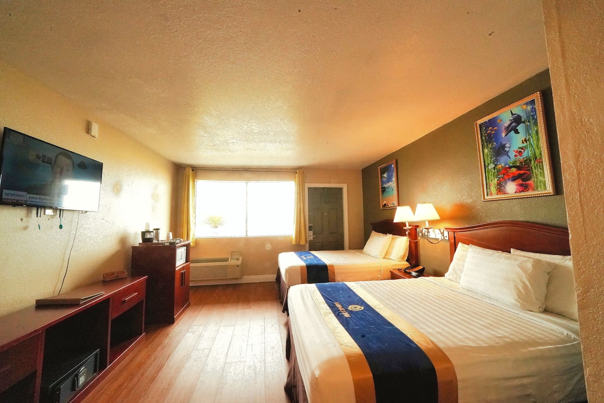 Hotellihuone, jossa on kaksi sänkyä, työpöytä, televisio ja taulu seinällä.