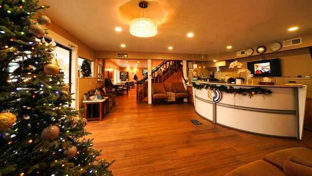 A warmly lit interior with a Christmas tree, a reception desk, and a staircase leading to upper floors. - Sandals Inn (Daytona Beach)