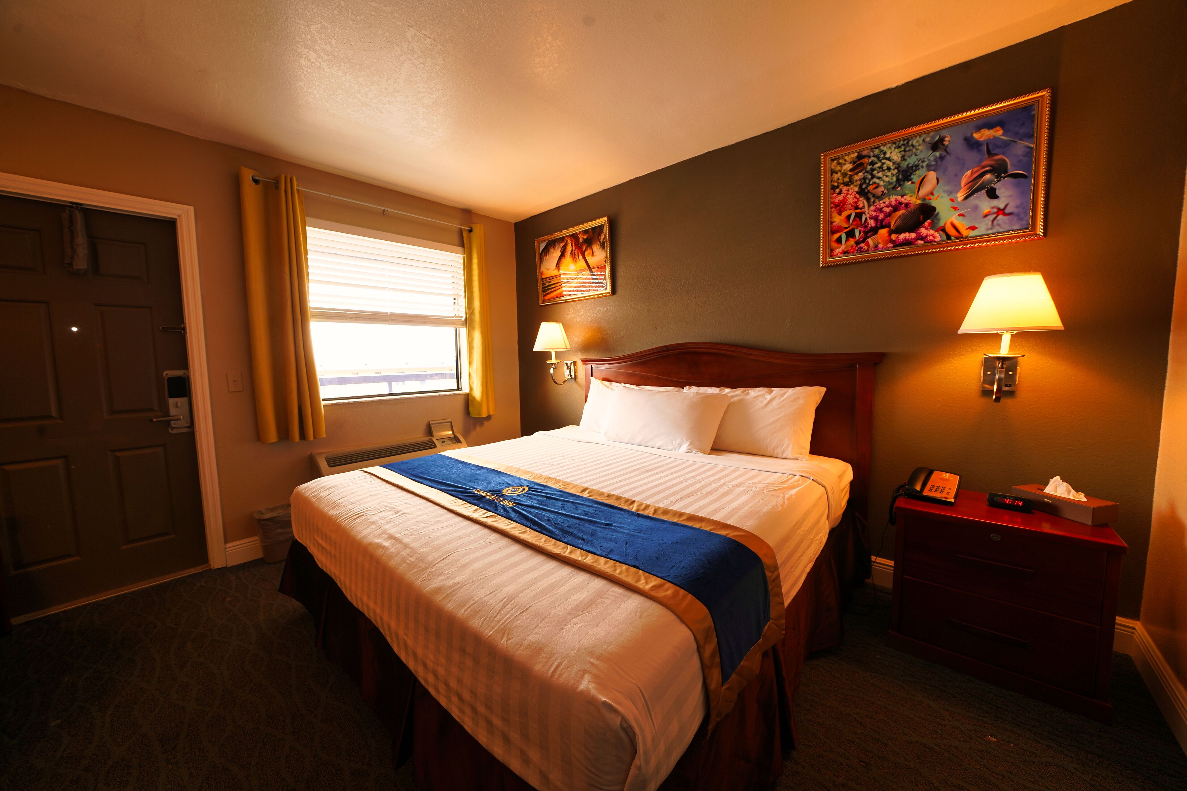 A hotel room with a large bed, two bedside lamps, a nightstand, a painting on the wall, and a window with curtains.