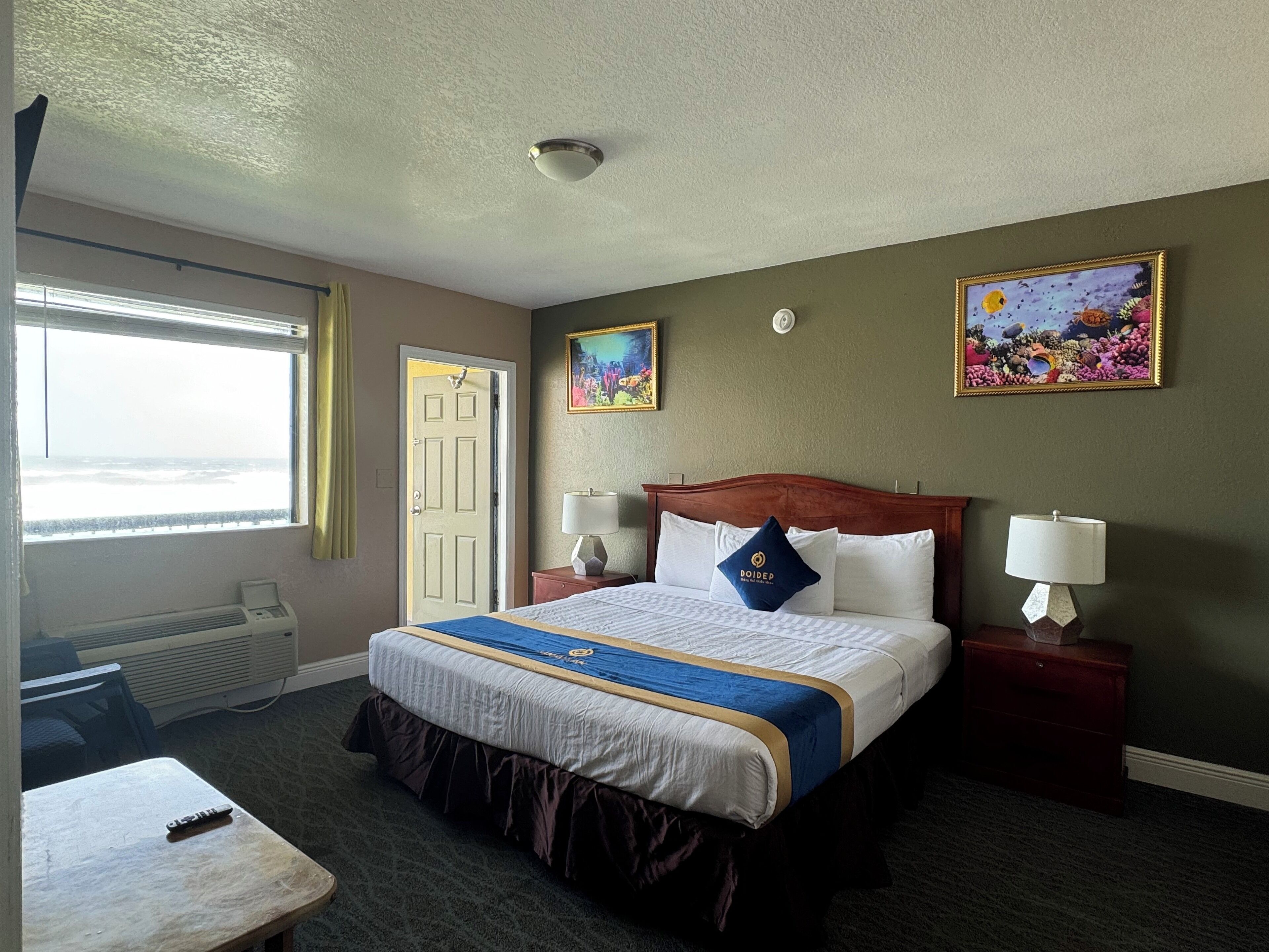 A hotel room with a large bed, two bedside lamps, a window with a view, a door, and a small table.