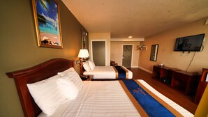 A hotel room with two beds, a TV, a desk, and a door leading to another room. - Sandals Inn (Daytona Beach)