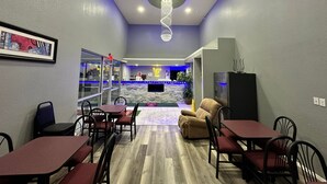Een restaurant met een modern interieur, met een centraal zitgedeelte met tafels en stoelen, een bar met een neonbord en een decoratieve lamp aan het plafond.