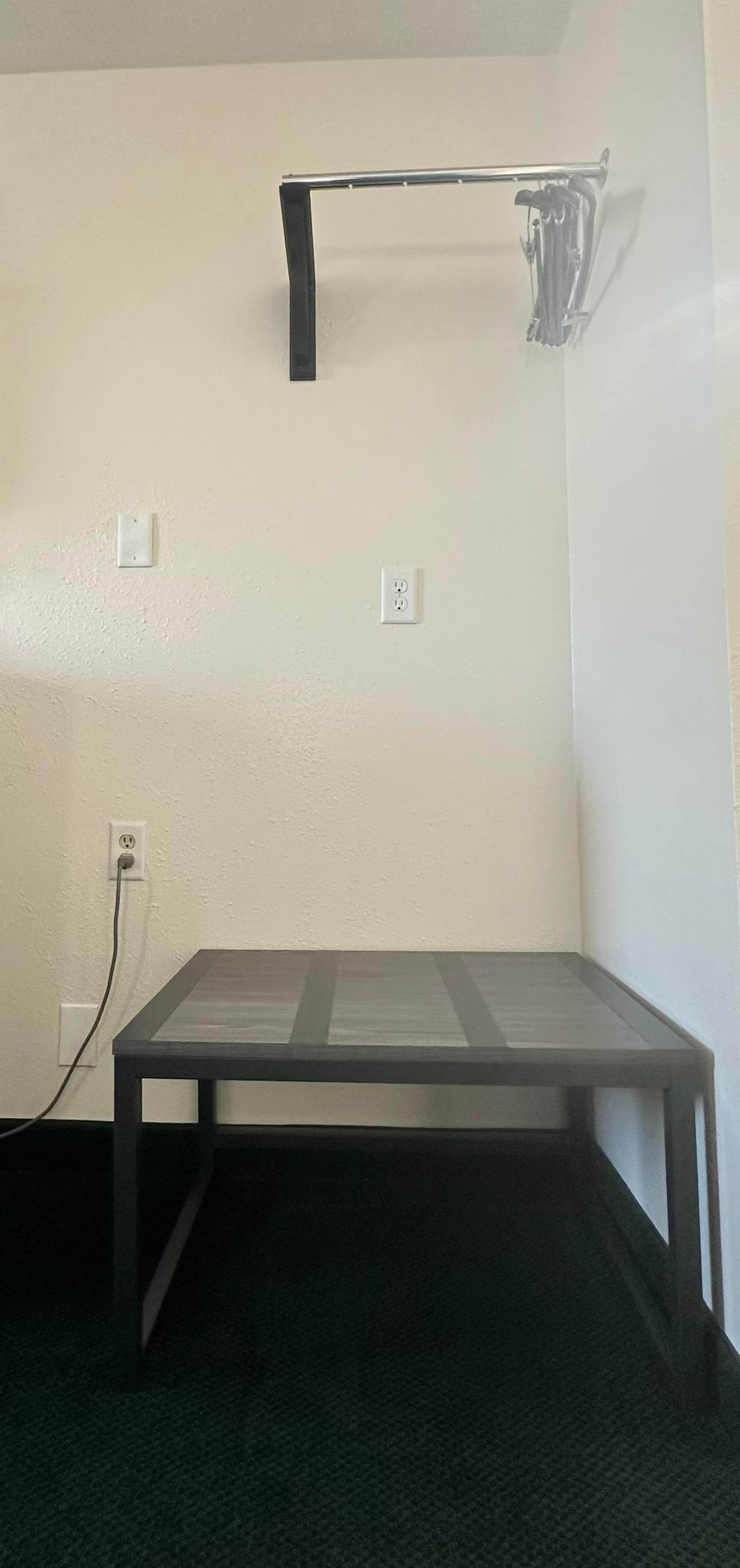A corner room with a small table, a power outlet, and a wall-mounted rack.