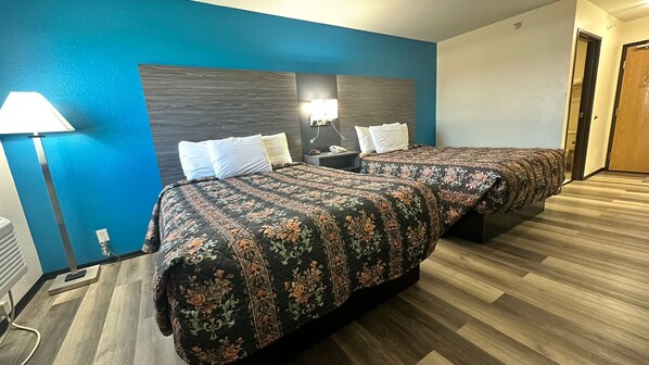 A hotel room with two beds, a nightstand, a lamp, and a wooden floor.