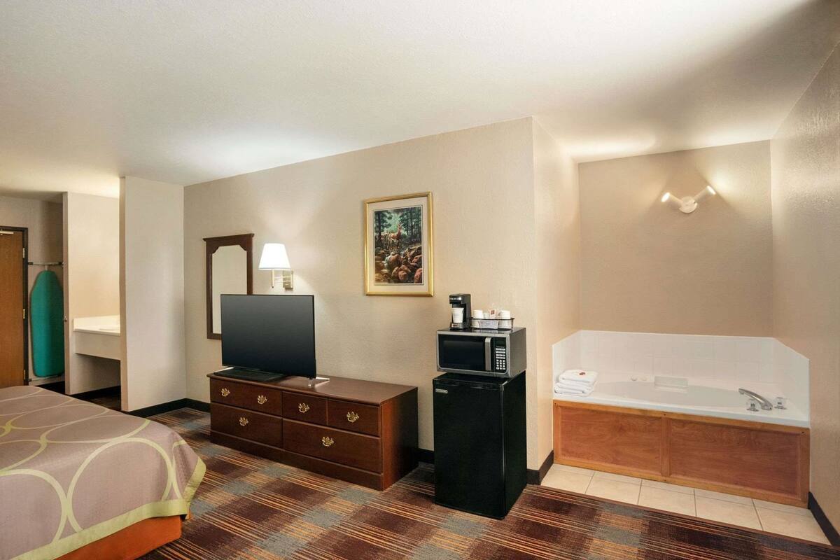 A hotel room with a bed, a desk with a lamp, a television, a microwave, and a bathtub.